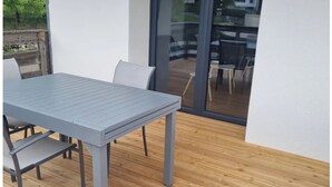 Moderni ulkotila, jossa on harmaa pöytä ja tuolit, puulattia sekä lasiovi, joka johtaa terassille.