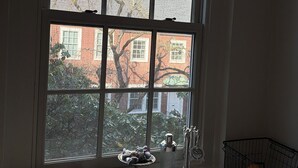 Ein Zimmer mit einem großen Fenster, einem kleinen Tisch mit Küchenutensilien und Blick auf Gebäude.