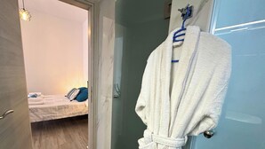 A hotel room with a bed, a white bathrobe hanging on a hook, and a towel rack with towels. - Black Sand Santorini Studio - 20m to Perissa Beach (Perissa)