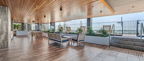 Een ruime binnenruimte met een houten plafond, een eethoek met stoelen en tafels, en uitzicht op de zee door grote ramen.