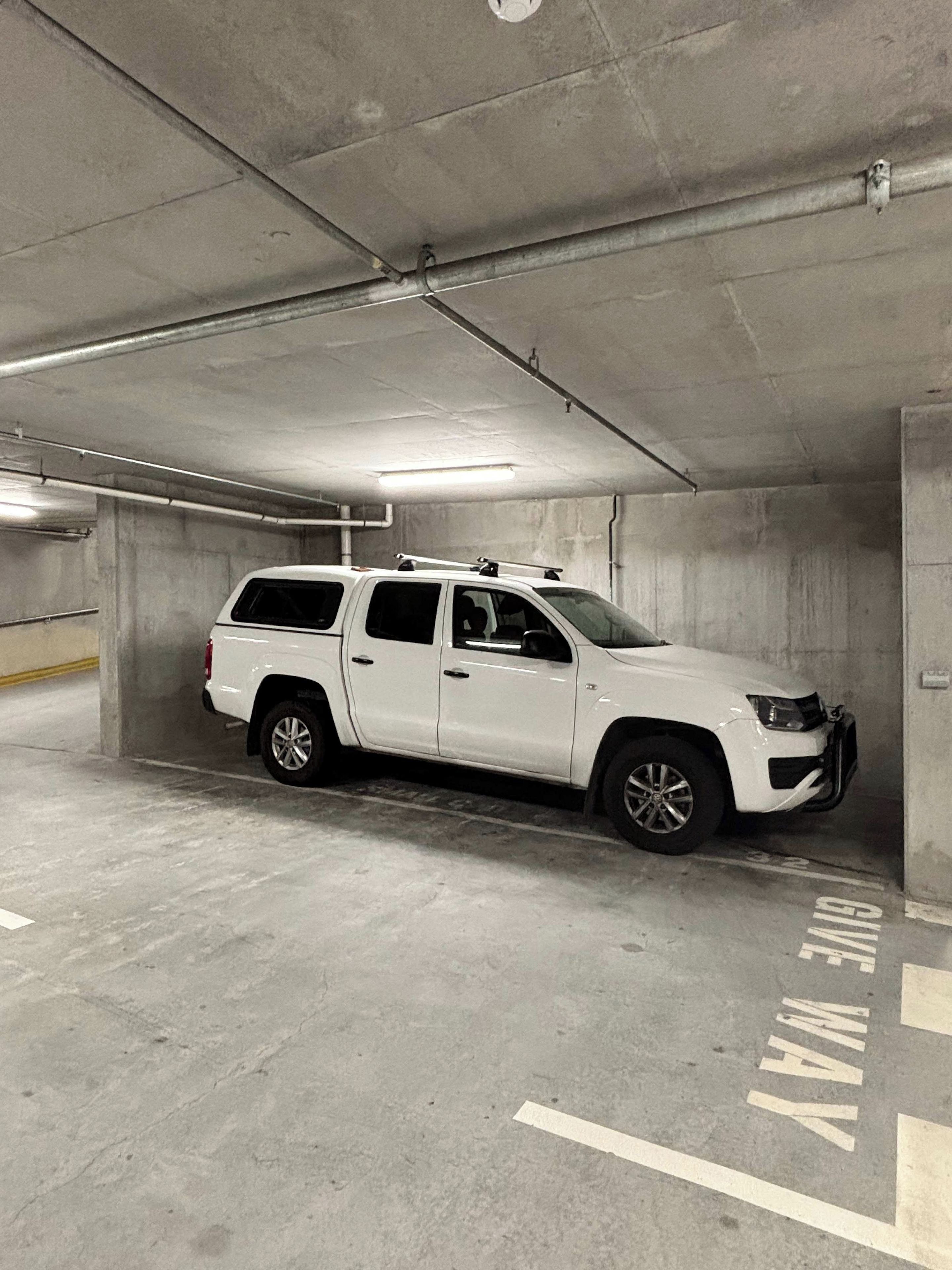 En hvid SUV parkeret i en beton parkeringsgarage med et skilt der siger 'FREE PARKING' på gulvet.