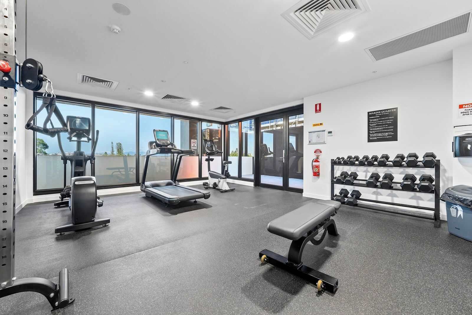A gym with treadmills, elliptical machines, a bench, and dumbbells.