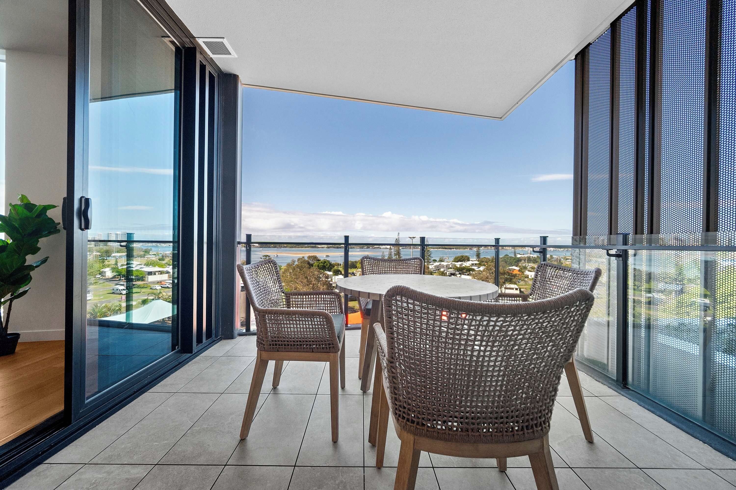 A balcony with a table and chairs, overlooking a coastal view.