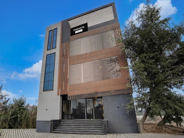 Un edificio moderno con un cartel que dice 'TOWNHOUSE', ventanas amplias y una escalera que conduce a la entrada.