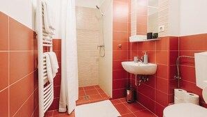 Une salle de bain avec des carreaux rouges, un lavabo blanc, une douche et des toilettes.