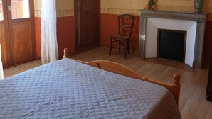 Een slaapkamer met een bed, een stoel, een open haard, een spiegel en een deur.