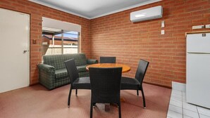 A room with a brick wall, a white air conditioner, a green sofa, a round table with chairs, and a white refrigerator. - Edithburgh Seaside Motel (Edithburgh)