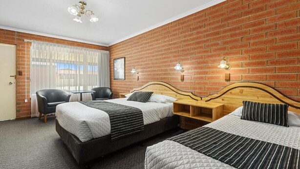A hotel room with two beds, a desk, a chair, and a brick wall. - Edithburgh Seaside Motel (Edithburgh)
