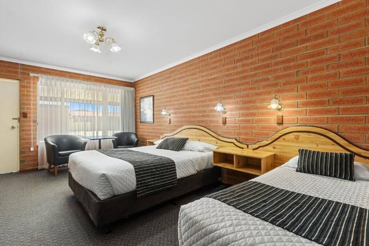 Habitación de hotel con dos camas, un escritorio, una silla y una pared de ladrillo.