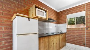 A kitchen with a brick wall, white refrigerator, wooden cabinets, and a window. - Edithburgh Seaside Motel (Edithburgh)