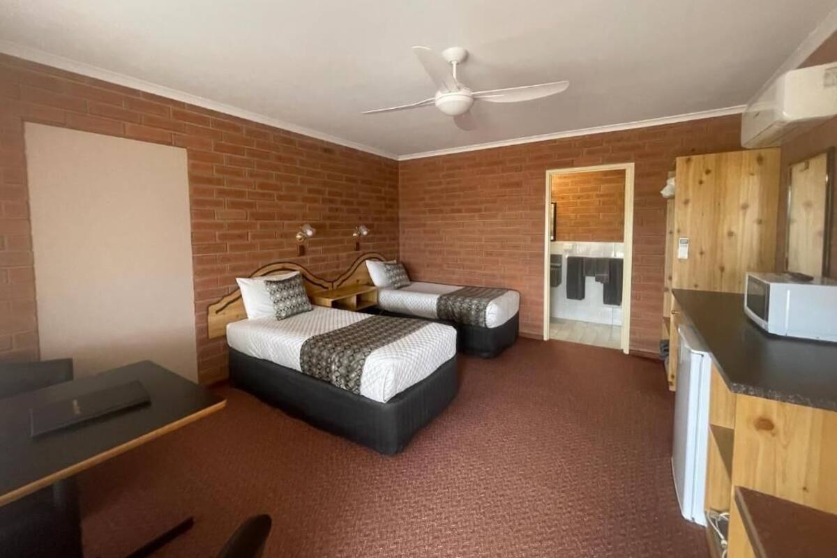 Una habitación con dos camas, un escritorio, una silla, un ventilador de techo y un microondas.