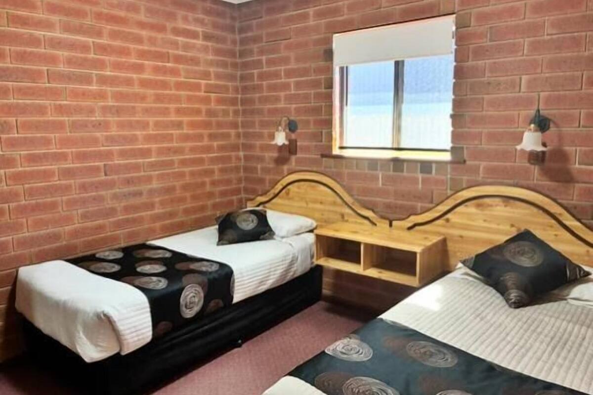Una habitación con paredes de ladrillo, dos camas con cabeceros, un ventanal y luces fijadas en la pared.