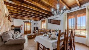 A rustic interior with exposed wooden beams, a dining table set for four, a sofa, and a fireplace.