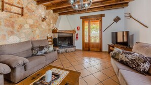 A living room with stone walls, wooden ceiling beams, a fireplace, a television, and two sofas.