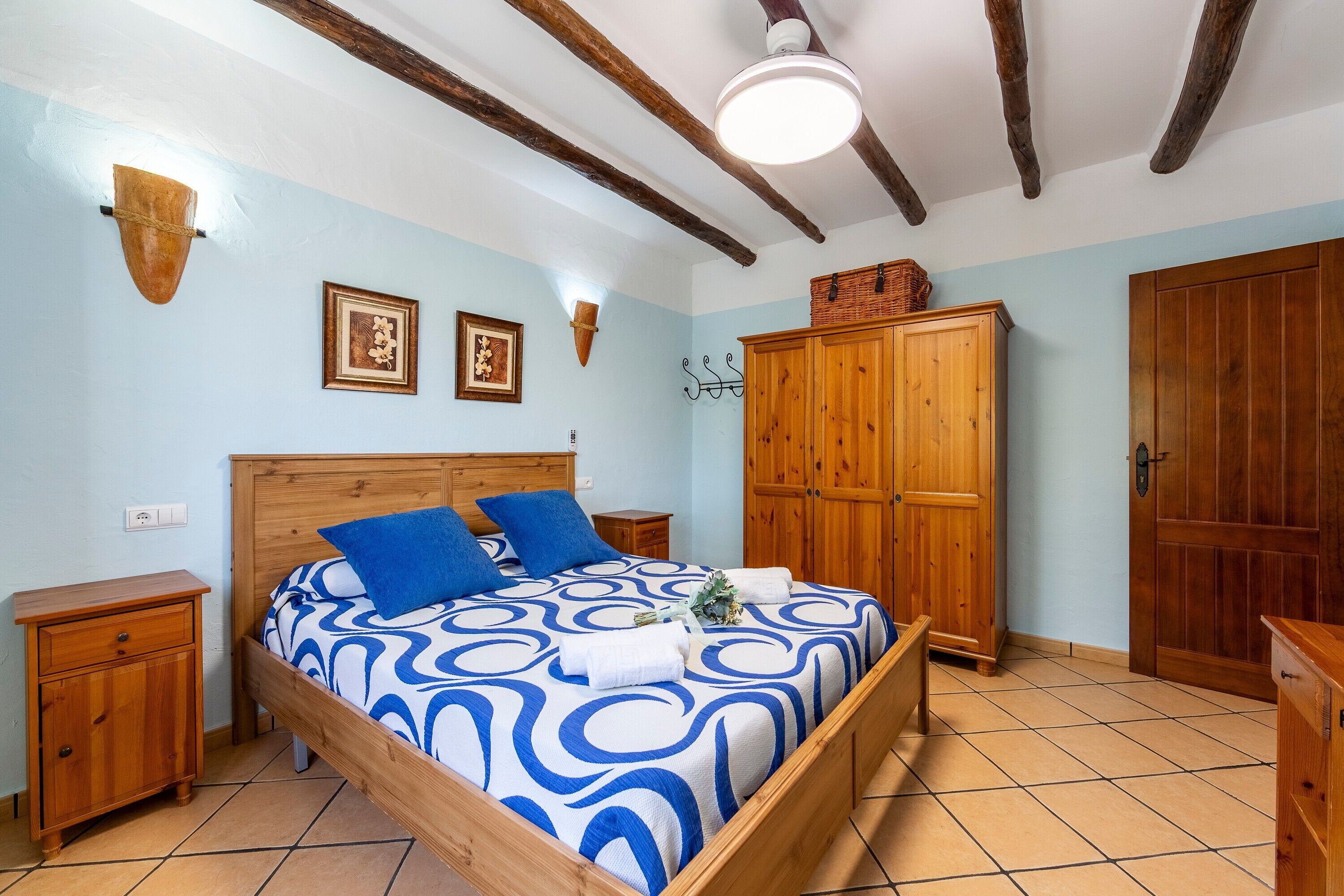 A bedroom with a wooden bed, a nightstand, a wardrobe, and a ceiling fan.
