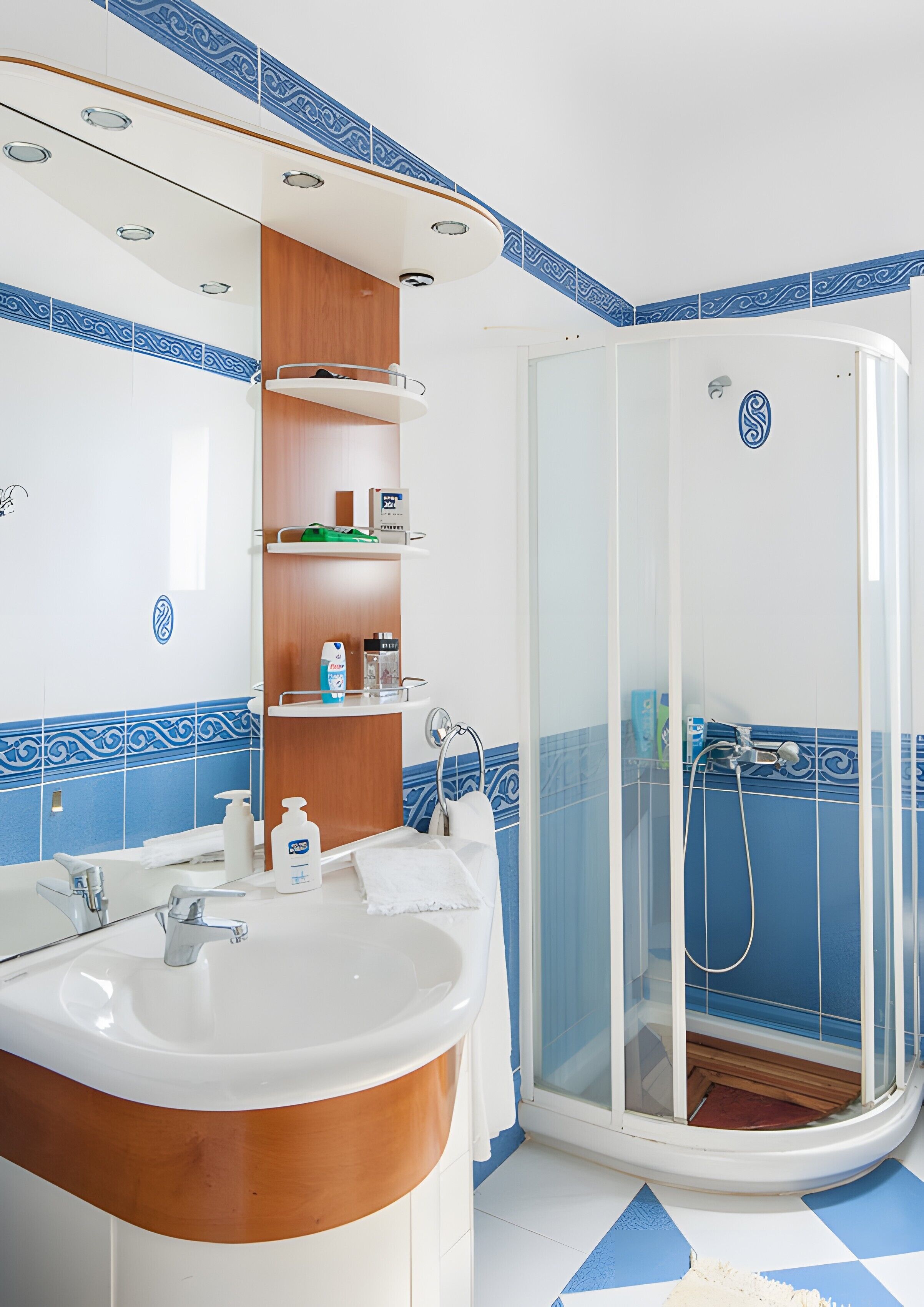 Un baño con un lavamanos curvo, un box de ducha de cristal y paredes con azulejos azules y blancos.