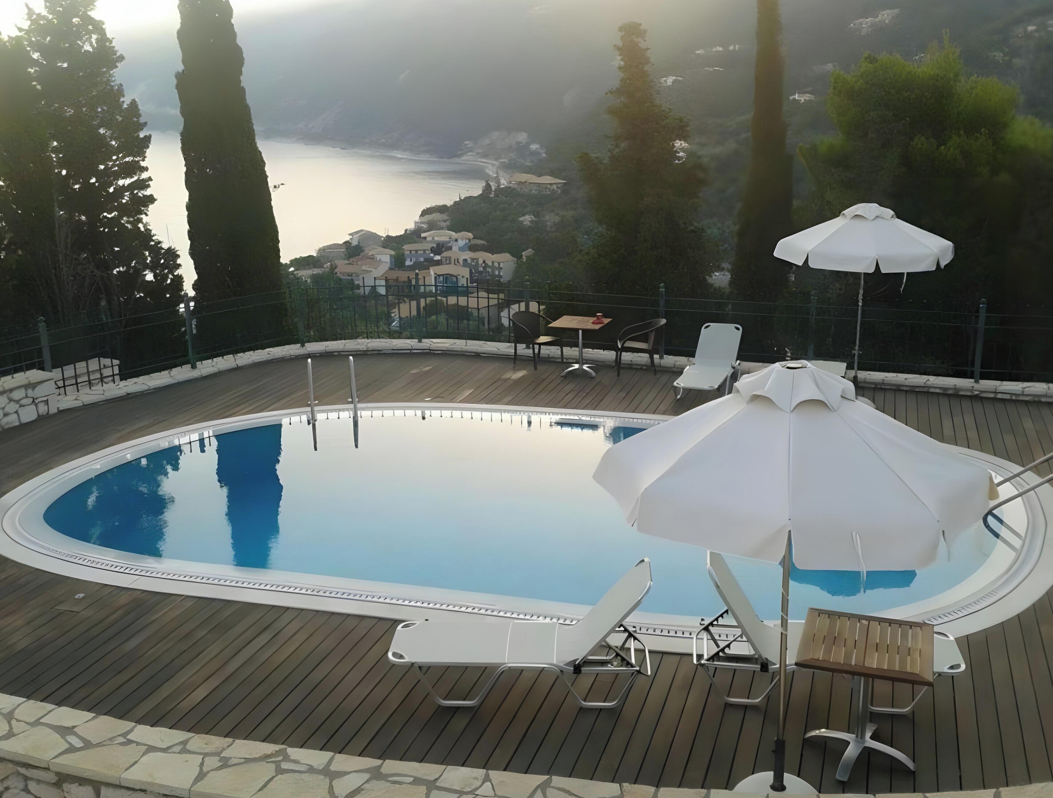 Piscina com espreguiçadeiras e guarda-sóis, cercada por um deck de madeira e uma borda de pedra.