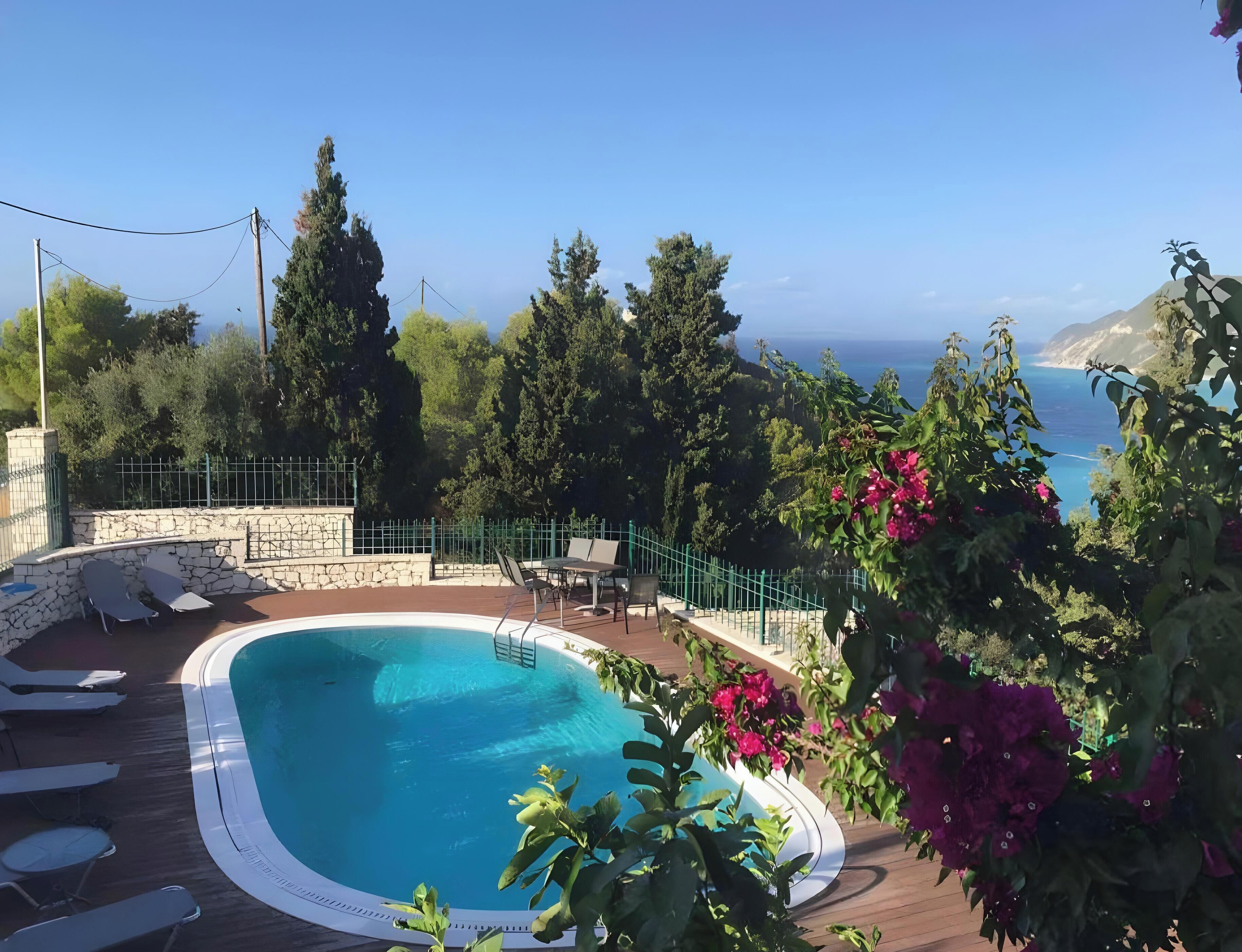 A swimming pool with lounge chairs, surrounded by greenery and a view of the sea.