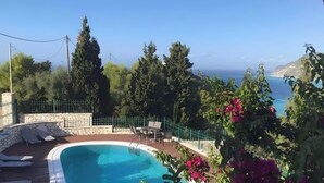 Uma piscina com espreguiçadeiras, rodeada por vegetação e vista para o mar.