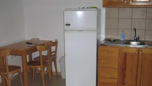 Uma cozinha compacta com geladeira, mesa de jantar de madeira, cadeiras e pia com torneira.