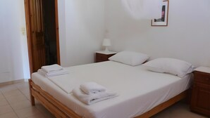Uma cama bem arrumada com lençóis e toalhas brancas, uma mesa de cabeceira com abajur e um criado-mudo de madeira.