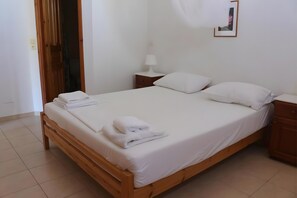 Ein ordentlich bezogenes Bett mit weißen Leinen und Handtüchern, ein Nachttisch mit Lampe und ein Holznachtkästchen.