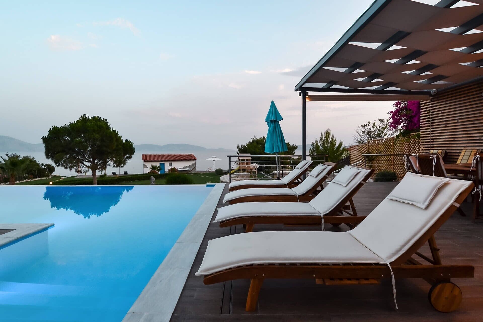 Un espace aménagé au bord de la piscine, avec des chaises longues, un coin salon abrité et une vue sur le paysage.