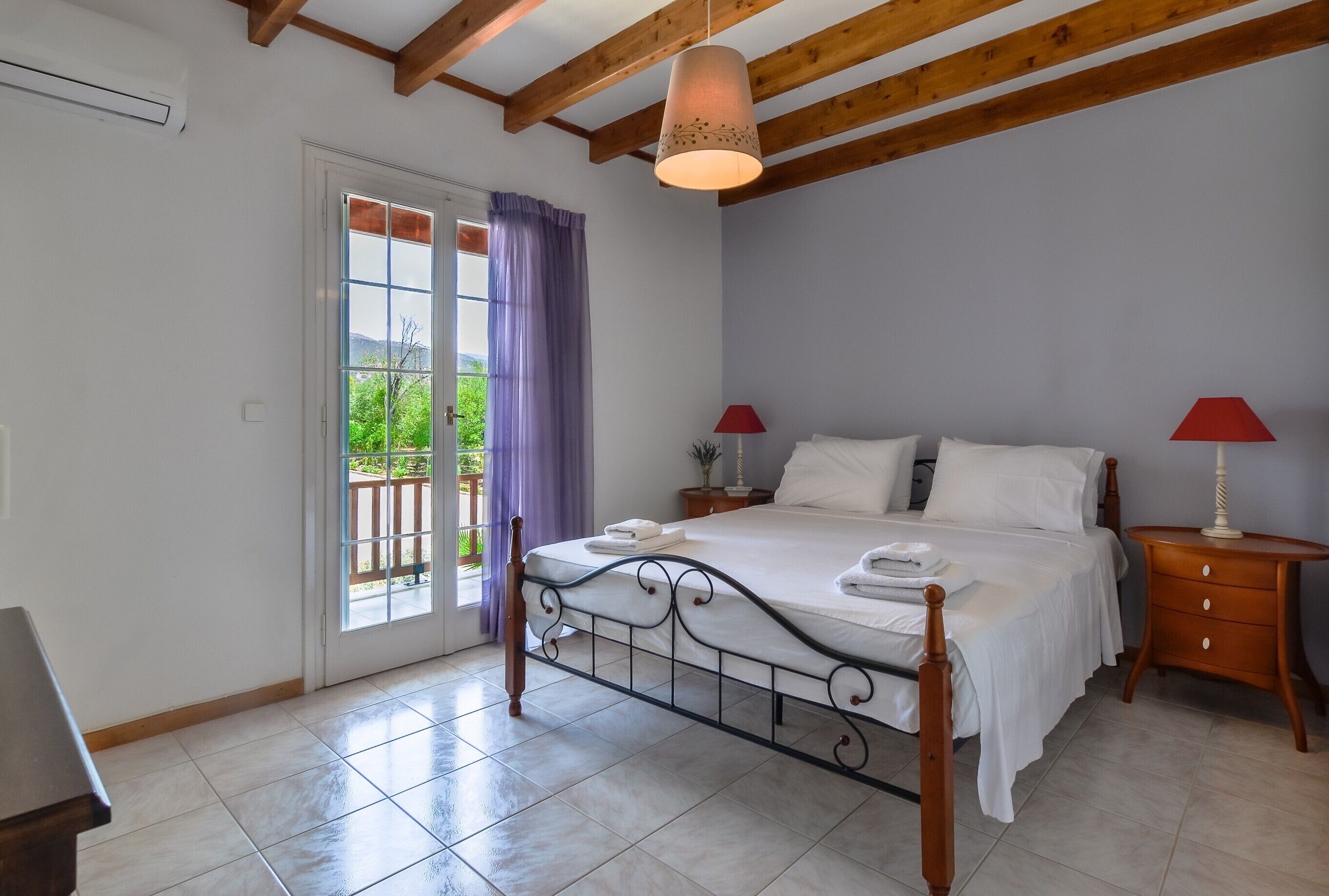 A bedroom with a bed, bedside tables, a window with curtains, and a view of greenery outside.