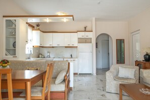 Una cocina moderna con armarios blancos, una mesa de comedor con sillas y una sala de estar con sofá y sillón.