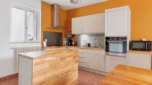 A kitchen with a wooden island, stainless steel appliances, and a window with a view. - Holiday Home 'Le Café De L'Encloître' with Private Terrace, Private Garden and Wi-Fi (Beaumont-Louestault)