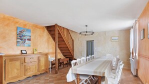A dining area with a long table, chairs, a wooden staircase, and a painting on the wall. - Holiday Home 'Le Café De L'Encloître' with Private Terrace, Private Garden and Wi-Fi (Beaumont-Louestault)