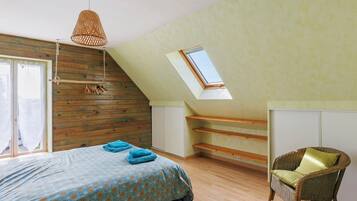 Une chambre avec un plafond en pente, un lit recouvert d’une couvre-lit à motifs, une chaise en osier et un puits de lumière.