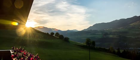 A view of a green landscape with mountains in the distance and a bright sun in the sky.