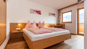 Un dormitorio con cama de madera, mesitas de noche, un ventanal con vistas y cuadros en la pared.