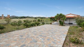 A paved pathway leading to a building with a red-tiled roof, surrounded by greenery and a clear sky.