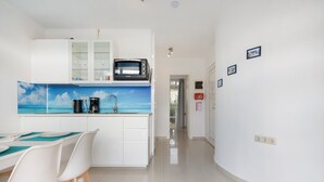 Une cuisine moderne équipée d’un four à micro-ondes, d’une machine à café et d’un pare-feu bleu. On y trouve un coin repas avec des chaises blanches et une table. La pièce est dotée de murs blancs et d’un sol carrelé.