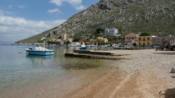 Un paysage côtier avec des bateaux, une plage rocheuse et des bâtiments situés sur une colline.