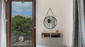 Une pièce dotée d’une porte-fenêtre coulissante, d’un miroir rond, d’une petite étagère ornée d’objets décoratifs et d’un pouf gris.