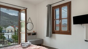 Une chambre avec un lit, un banc, une télévision et une vue sur une montagne et des bâtiments.