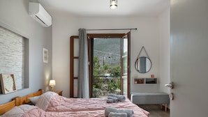 Une chambre avec un grand lit, une table de chevet avec une lampe, une fenêtre donnant sur une montagne et un petit banc.
