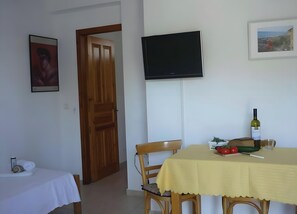 Ein Zimmer mit einem Bett, einem Tisch mit gelber Tischdecke, einem Fernseher und einer Tür.