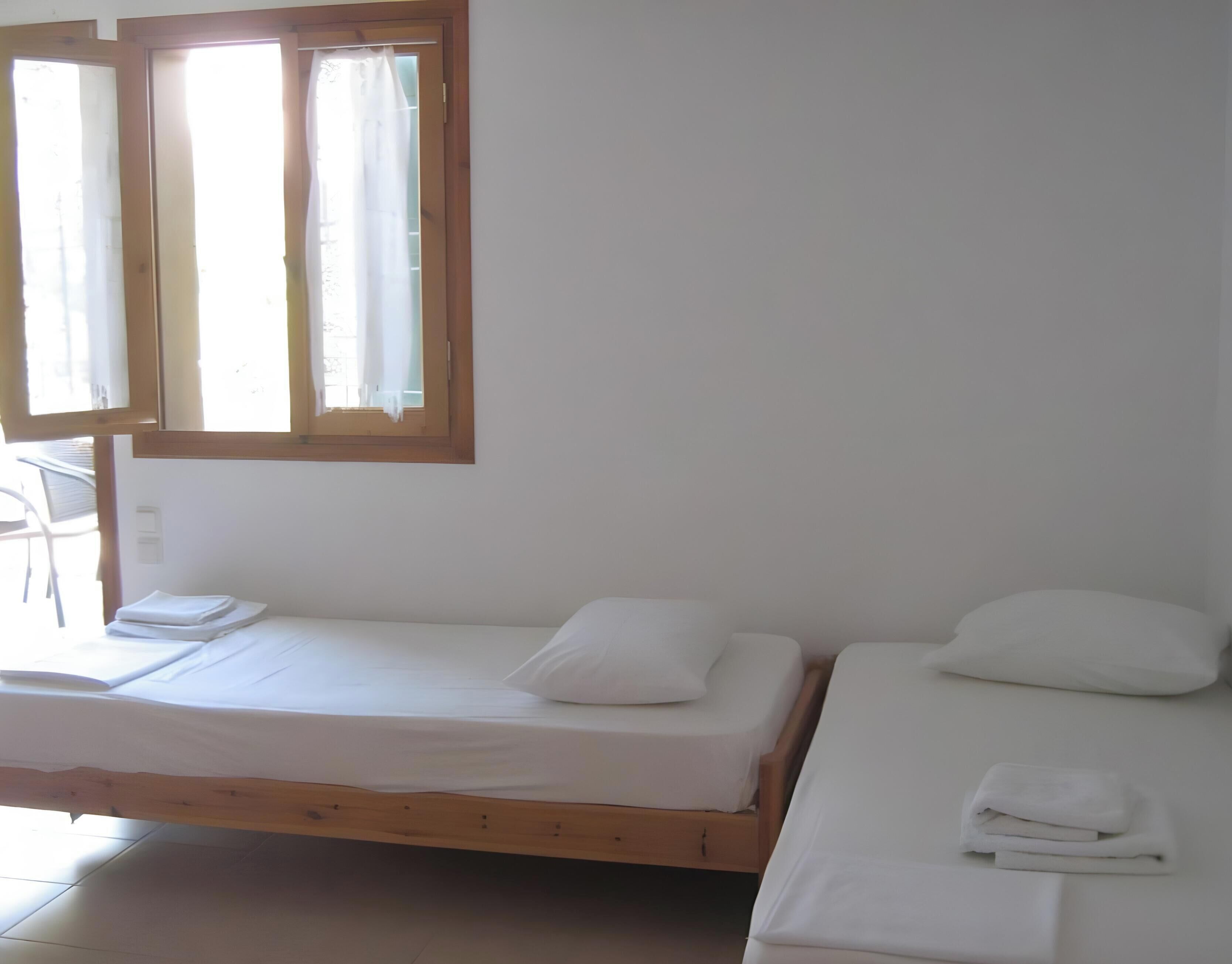 A room with two single beds, a window with curtains, a chair, and a small table.