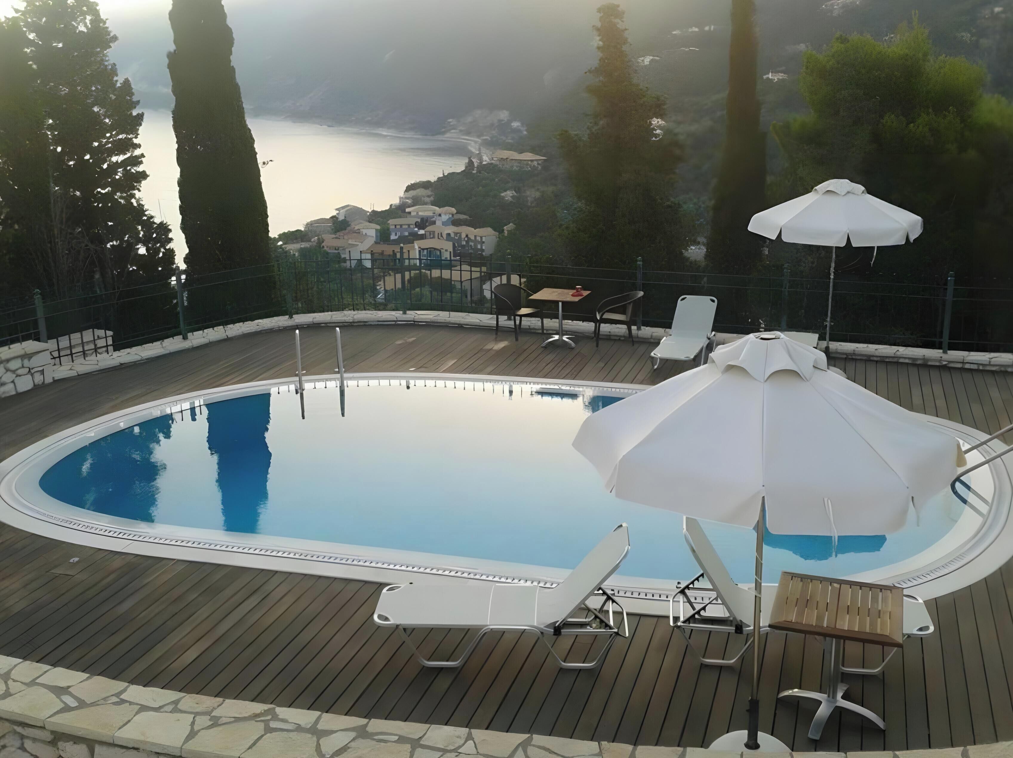 Piscina com espreguiçadeiras e guarda-sóis, cercada por um deck de madeira e uma borda de pedra.