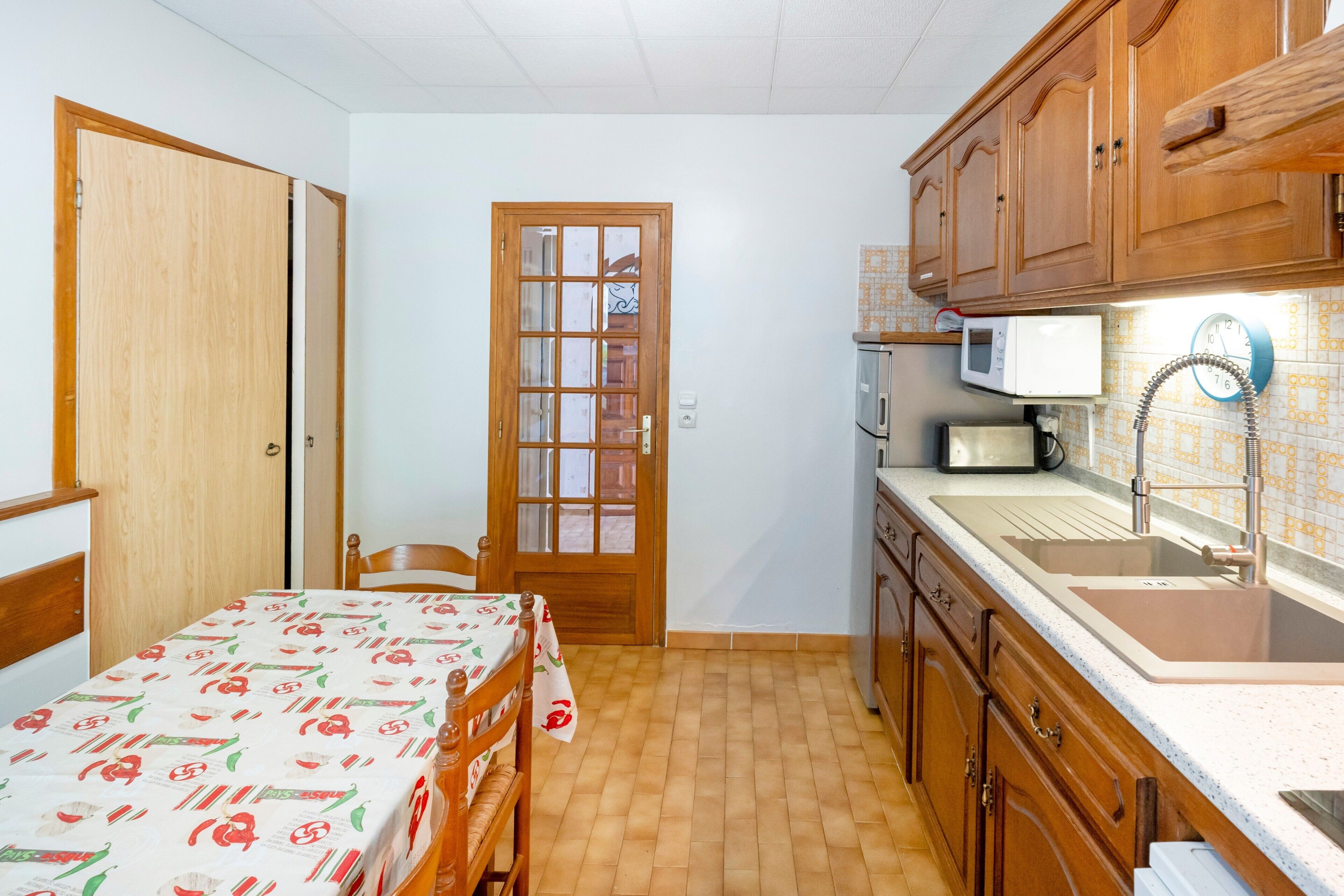 Una cocina funcional con armarios de madera, un microondas, un fregadero y una zona de comedor con mesa y sillas.