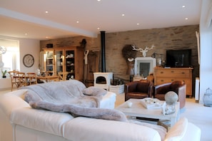 A living room with a sofa, a coffee table, a fireplace, a television, and a stone wall. - Harborfront Seaside House with Port View (Le Conquet)