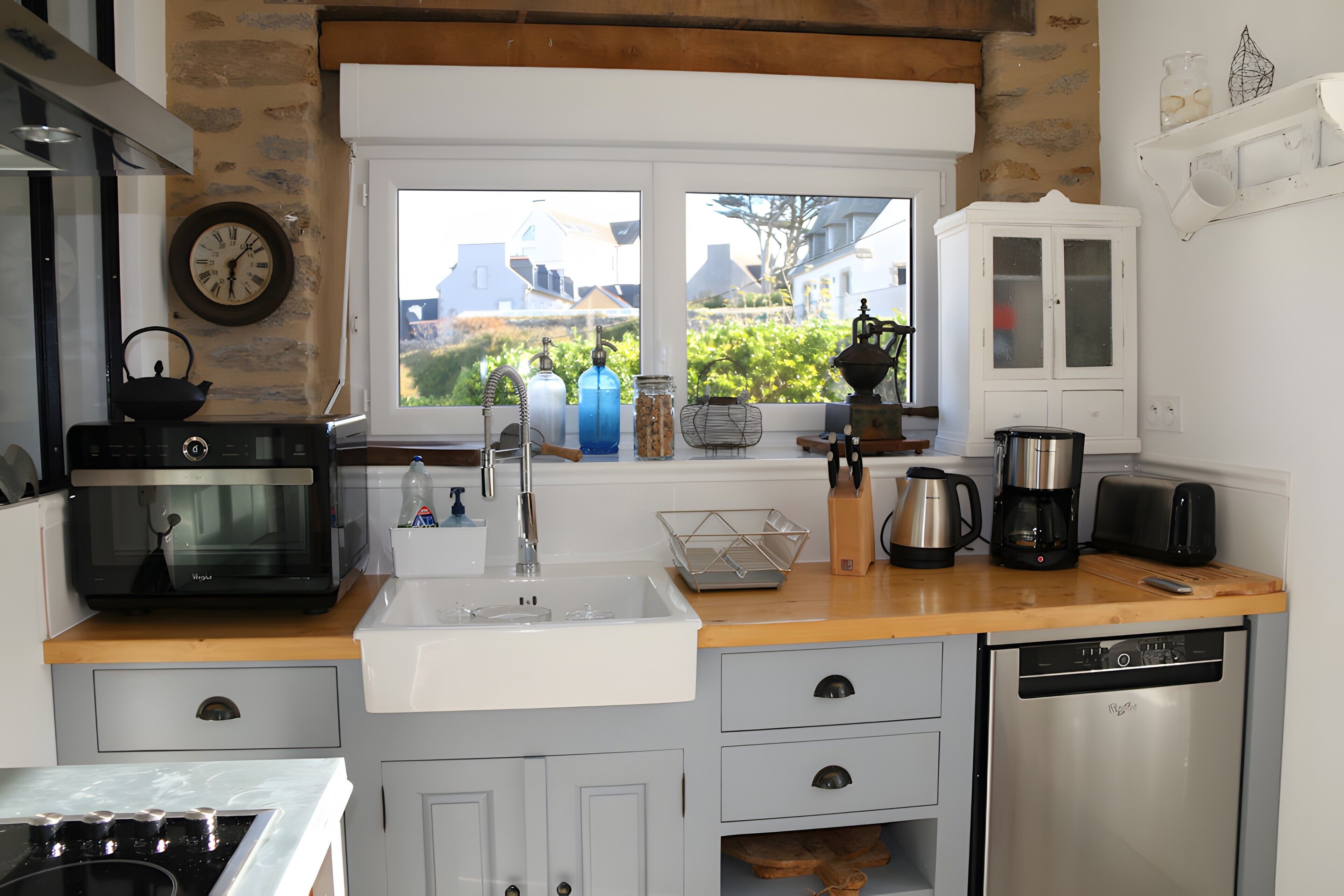 Een keuken met een spoelbak, fornuis, oven en een raam met uitzicht op huizen.