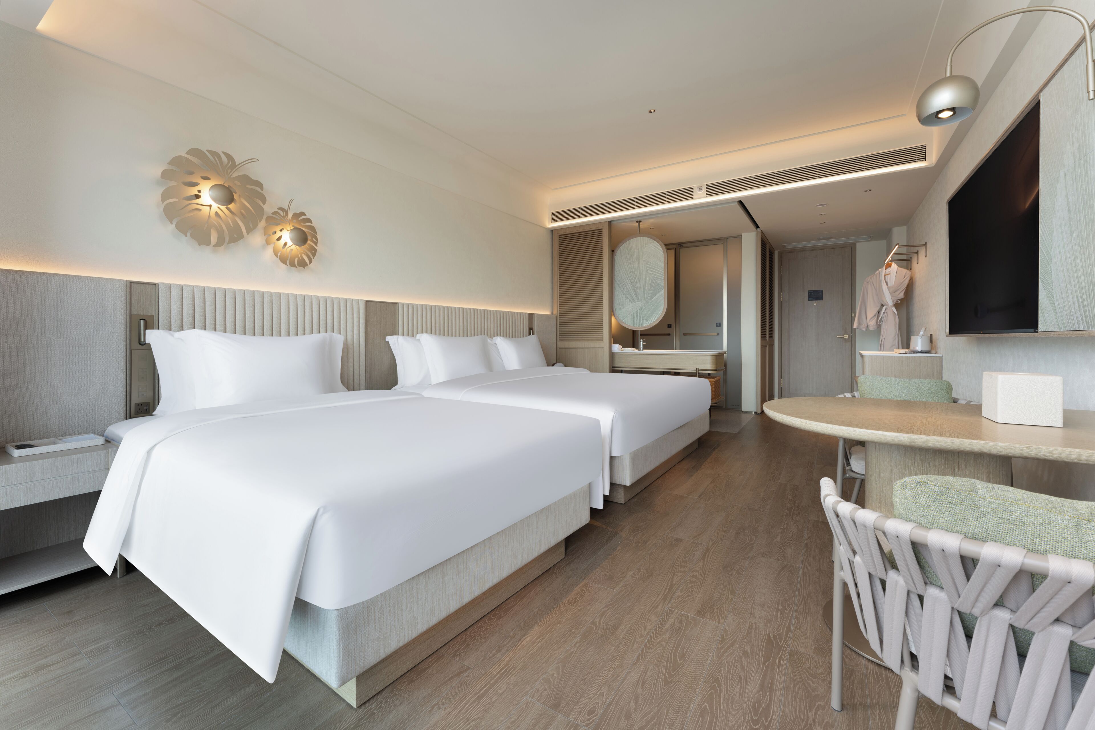 A modern hotel room with two beds, a sitting area, a vanity with a mirror, and a television.