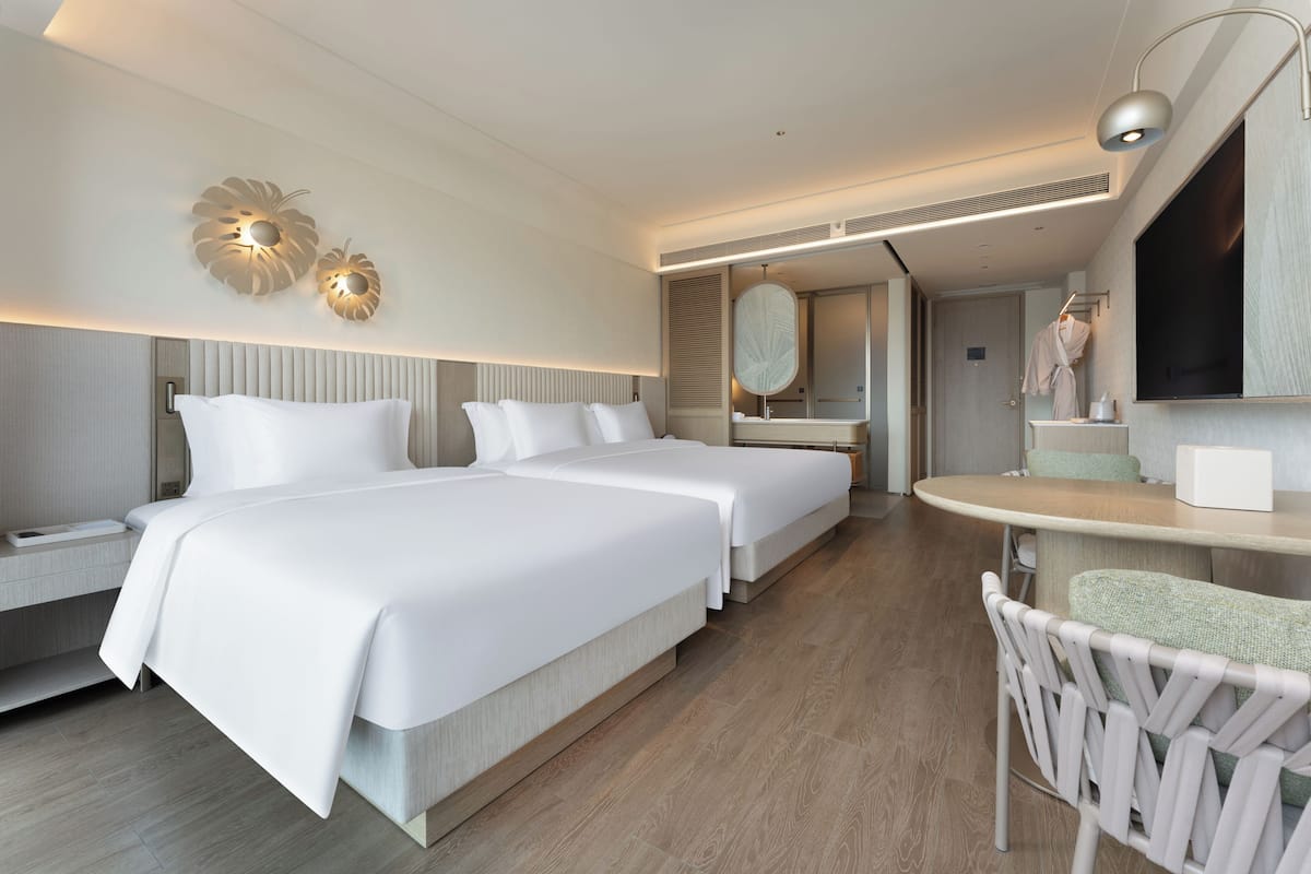 Ein modernes Hotelzimmer mit zwei Betten, einer Sitzecke, einem Schminktisch mit Spiegel und einem Fernseher.