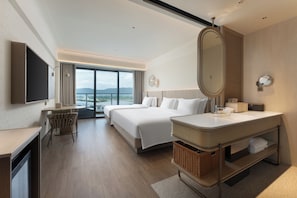 A hotel room with a bed, a desk, a TV, a large window, and a bathroom with a mirror and sink.