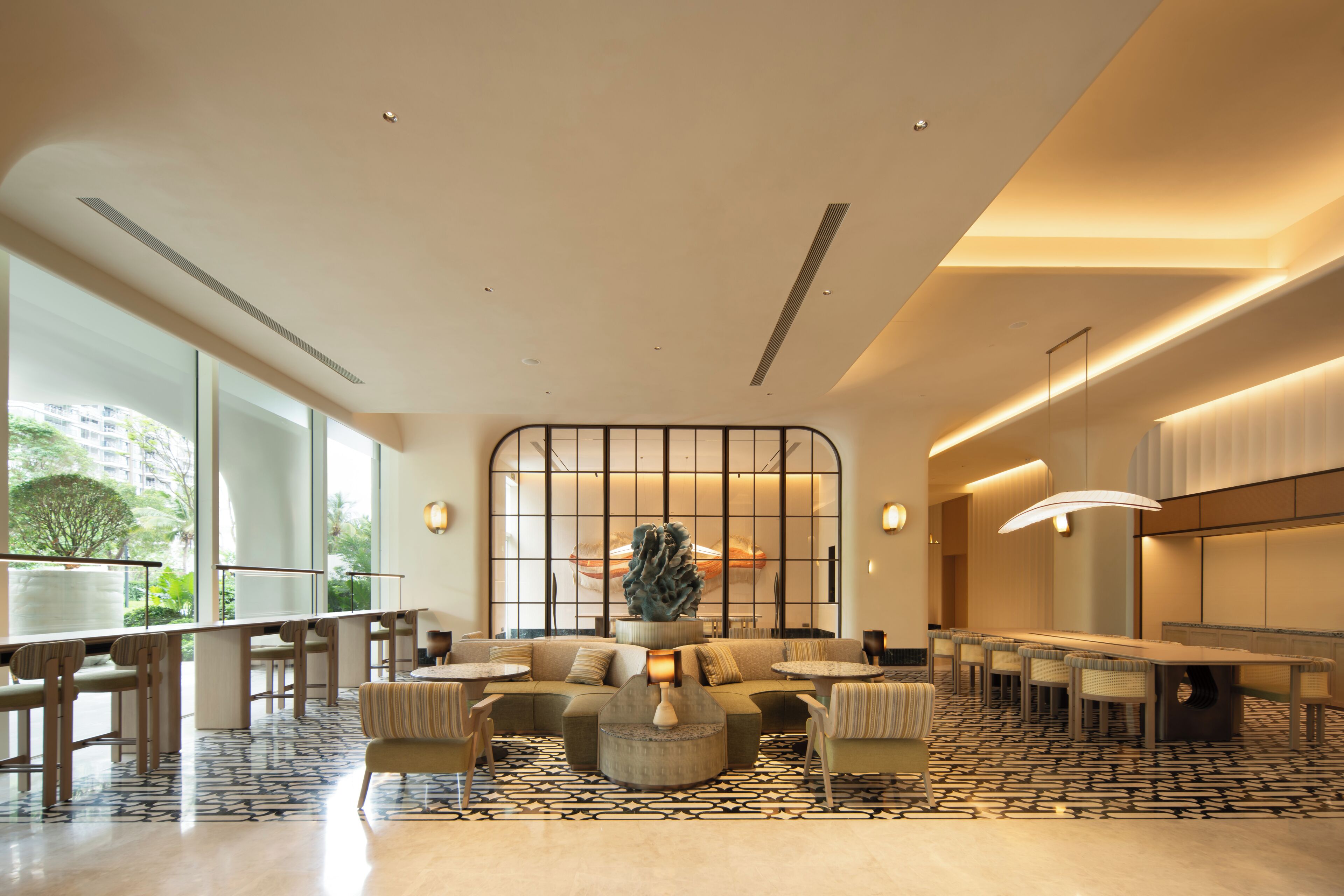 A modern hotel lobby with a seating area, a reception desk, and large windows offering a view of the outdoors.